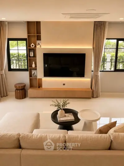 Elegant living room with modern decor, large TV, and natural light from windows.