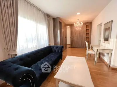 Elegant living room with plush navy sofa, chandelier, and wooden flooring.