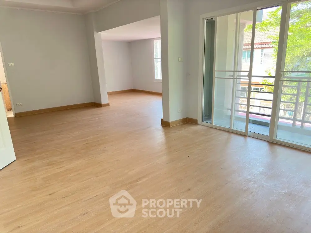 Spacious and sunlit living room with gleaming hardwood floors leading to a cozy balcony with a serene view, perfect for modern living.