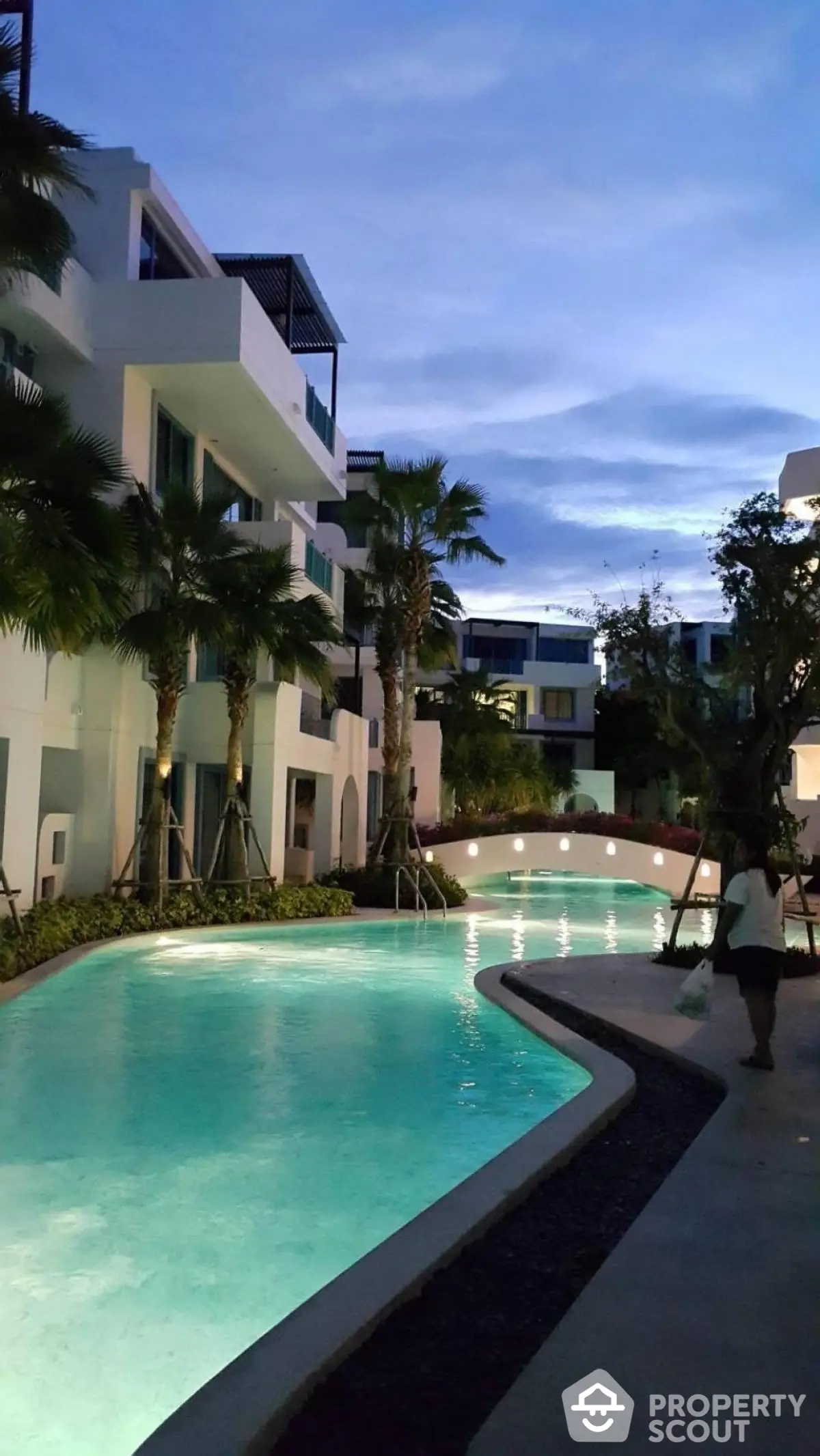 Luxurious residential complex with illuminated pool and modern architecture at dusk.