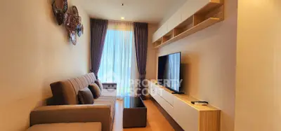 Modern living room with stylish decor, large TV, and natural light through floor-to-ceiling windows.