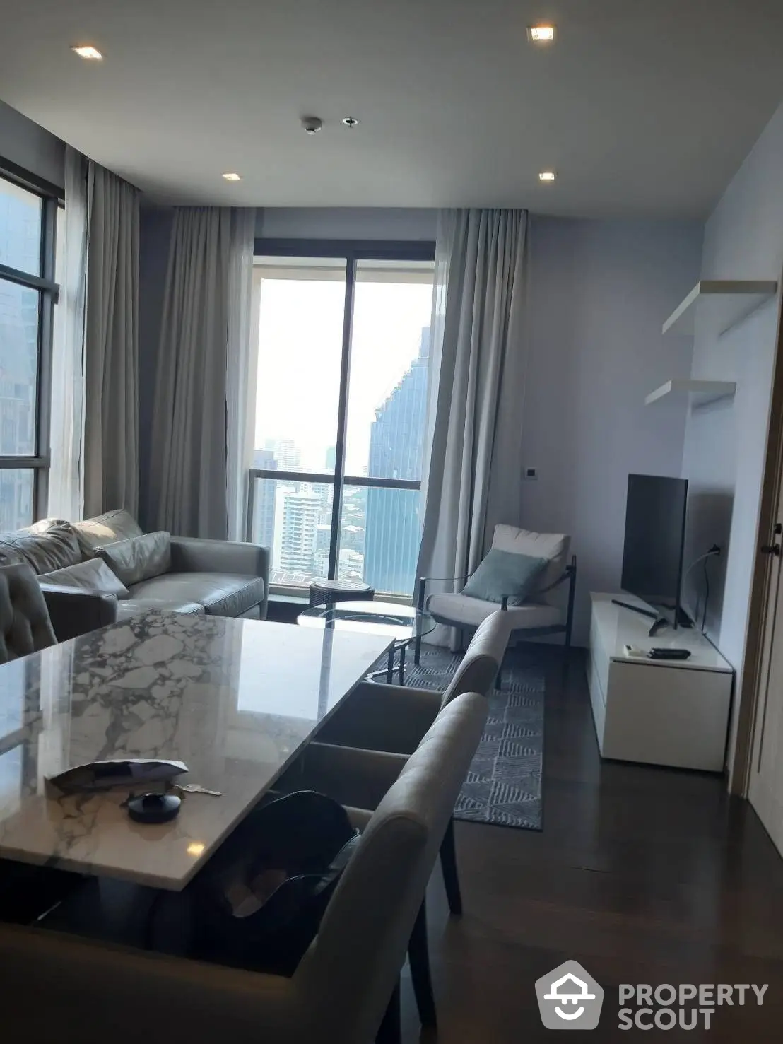 Luxurious high-rise living room with floor-to-ceiling windows offering a panoramic city view, elegant marble dining table, and plush seating.