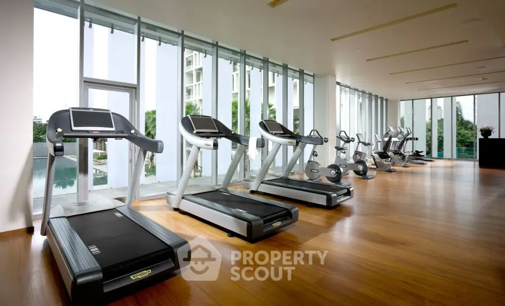 Modern gym with treadmills and large windows overlooking a pool in luxury apartment complex.