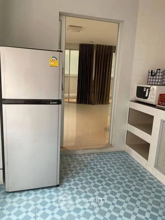 Modern kitchen with sleek fridge and tiled flooring, leading to a spacious balcony.