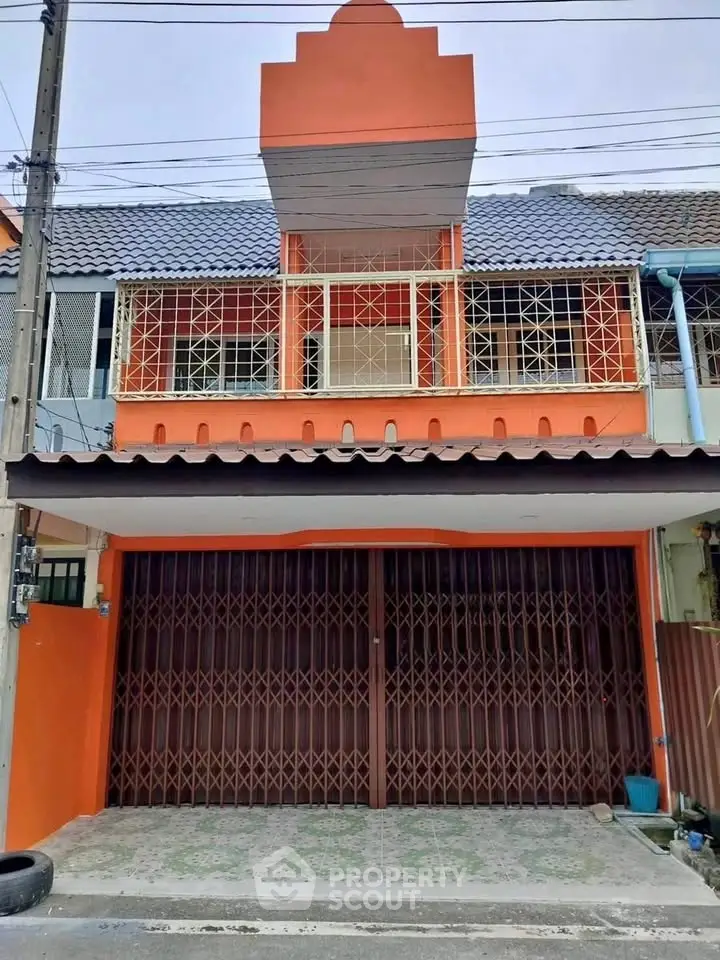 Charming two-story townhouse with vibrant orange facade and secure gated entrance.