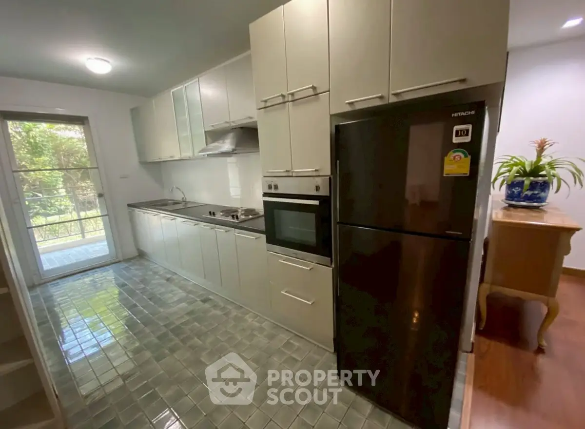 Modern kitchen with sleek cabinetry and large fridge, featuring a bright window view.
