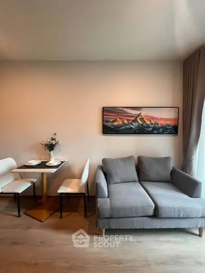 Modern living room with cozy gray sofa and elegant dining area, featuring mountain artwork and natural light.