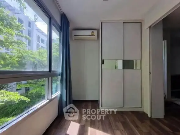 Bright bedroom with large window and modern sliding closet doors, featuring air conditioning and wooden flooring.