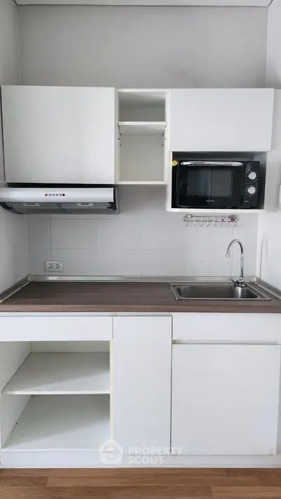 Compact kitchen with white cabinets and built-in microwave, ideal for modern apartments.