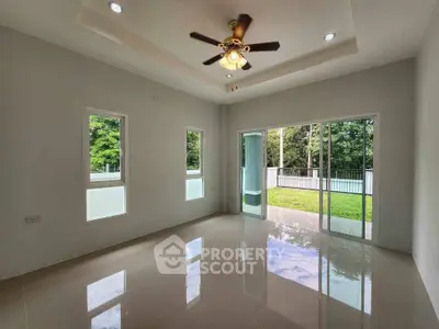 Spacious living room with ceiling fan and large windows overlooking lush garden.