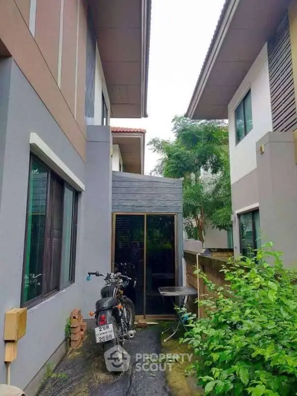 Modern residential exterior with lush greenery and motorcycle parking.