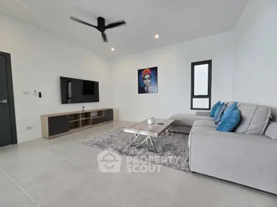 Modern living room with sleek furniture and wall art, featuring a ceiling fan and large TV.