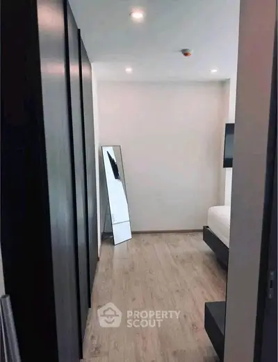 Modern bedroom with sleek design and wooden flooring, featuring a large mirror and ambient lighting.