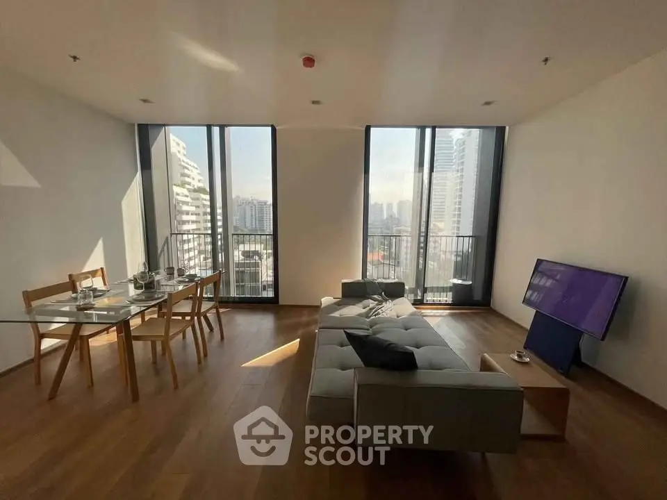 Spacious modern living room with large windows and city view, featuring a cozy sofa and dining area.