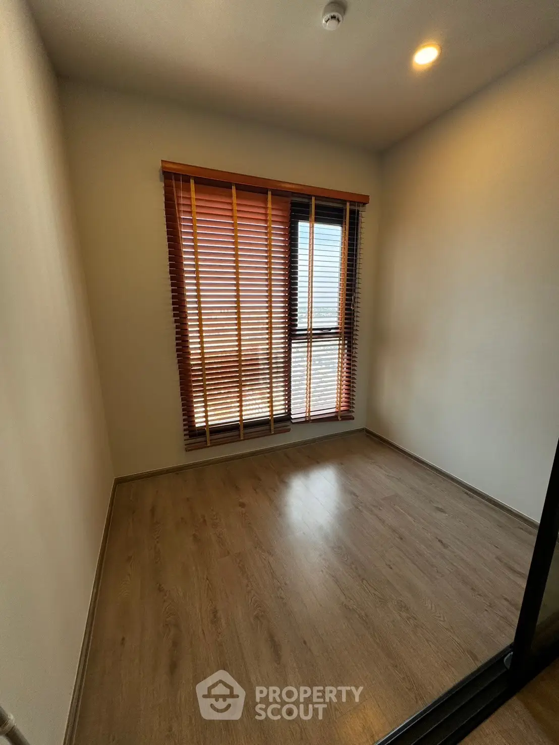 Cozy empty room with wooden flooring and large window with blinds, perfect for customization.