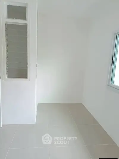 Bright empty room with tiled flooring and large window, perfect for customization.
