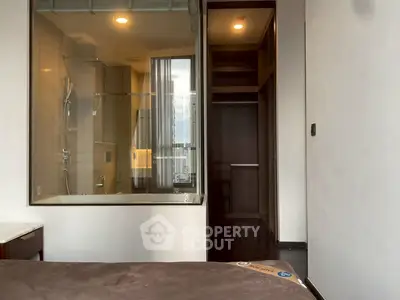 Modern bedroom with glass-walled bathroom and city view, featuring sleek design and contemporary finishes.