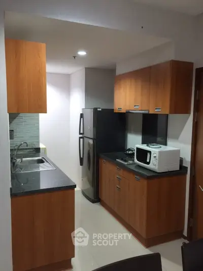 Modern kitchen with wooden cabinets, sleek countertops, and appliances including a microwave and fridge.