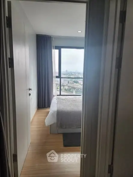 Modern bedroom with city view and natural light through large window.
