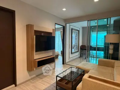 Modern living room with TV, glass coffee table, and view of city skyline from balcony.