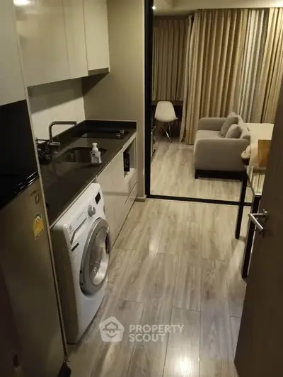 Modern compact kitchen with washing machine and cozy living area in stylish apartment.