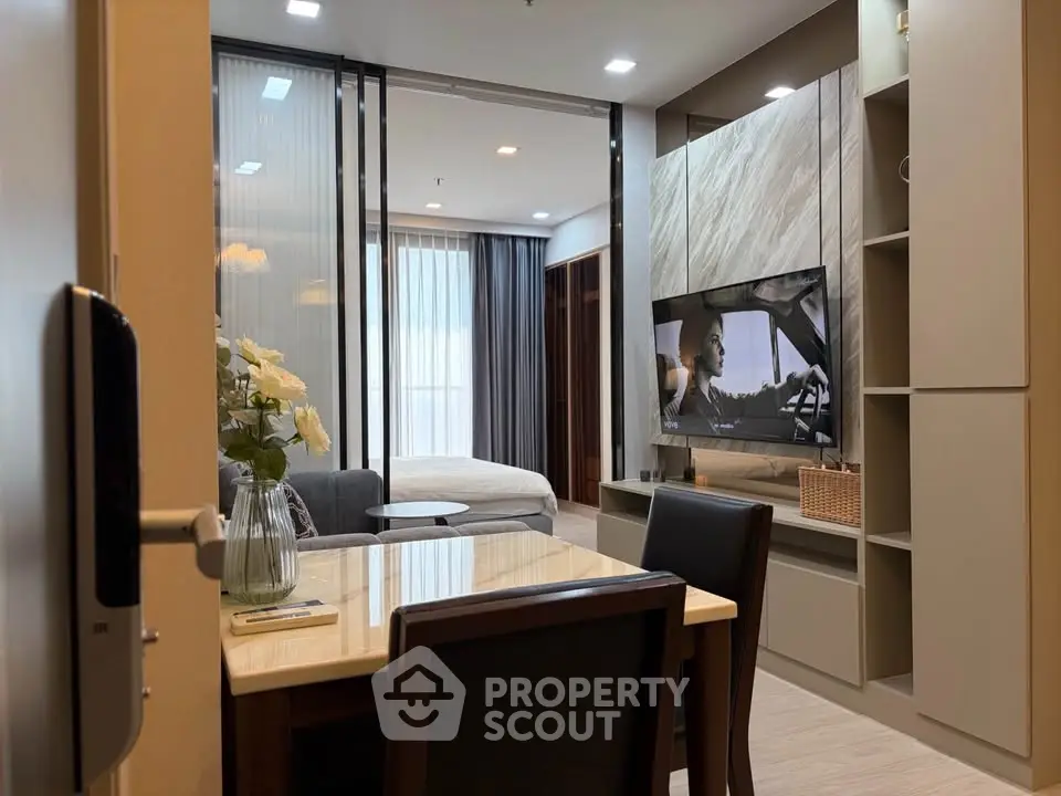 Modern open-plan living room with stylish decor and large TV, leading to a cozy bedroom area.