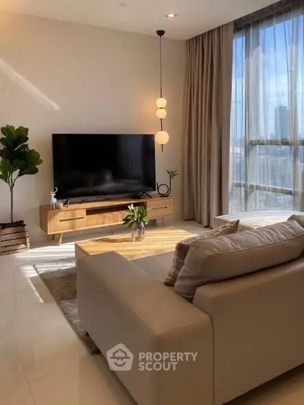 Modern living room with large TV, stylish furniture, and floor-to-ceiling windows offering natural light.