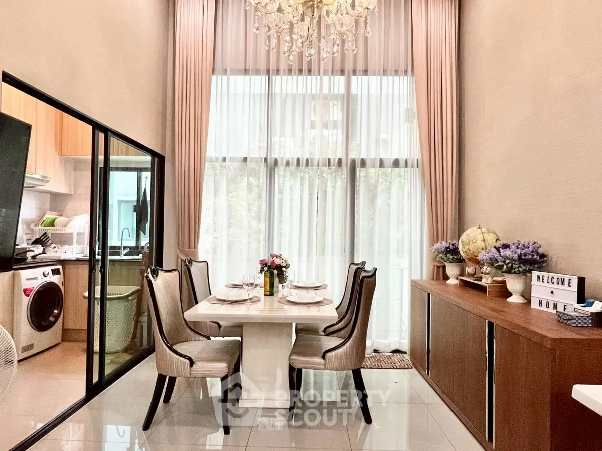 Elegant dining area with high ceilings and chandelier, adjacent to a modern kitchen with washing machine.