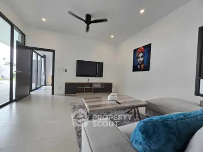 Modern living room with sleek furniture and wall art, featuring a ceiling fan and large TV.