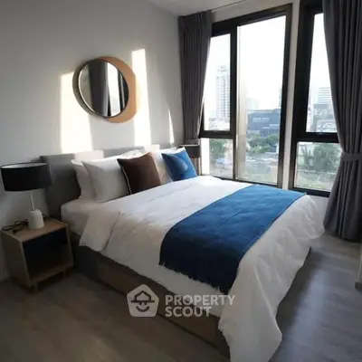 Modern bedroom with large windows offering ample natural light and a stunning city view, complemented by stylish furnishings and a cozy color palette.