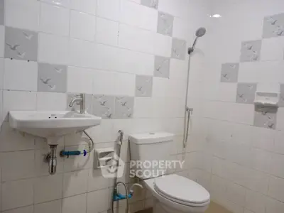 Modern bathroom with white tiles, shower, sink, and toilet in a minimalist design.