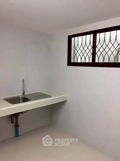 Minimalist kitchen with sleek countertop and modern sink under decorative window.