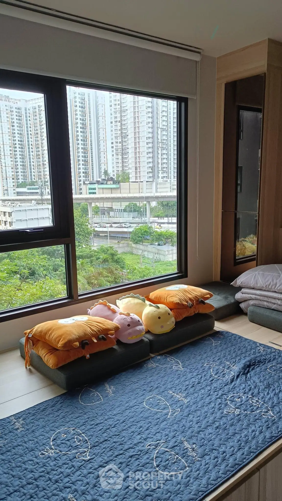 Cozy bedroom with large window offering stunning cityscape views, perfect for relaxation and comfort.