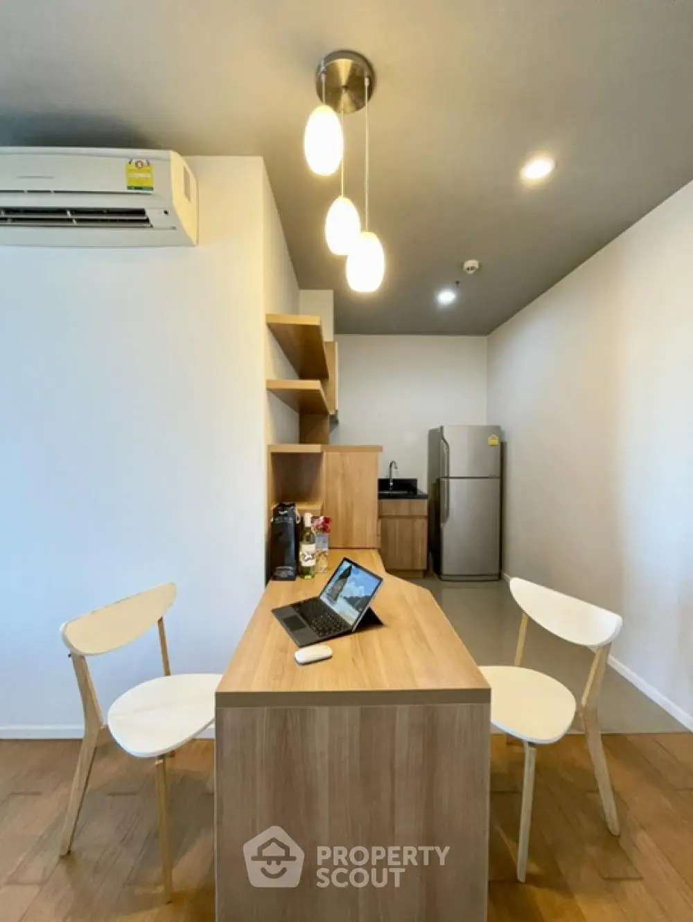 Modern kitchen with sleek wooden dining table and chairs, featuring contemporary lighting and stainless steel fridge.