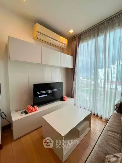 Modern living room with sleek furniture and large window offering city views.