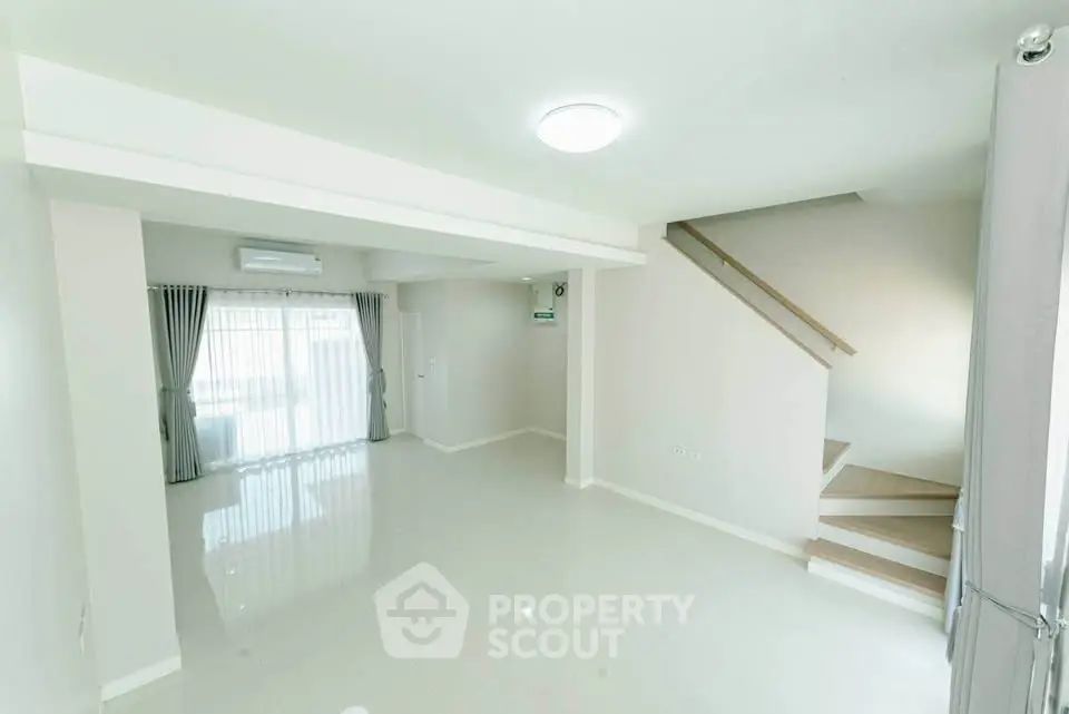 Spacious modern living room with staircase and large window, perfect for family gatherings.