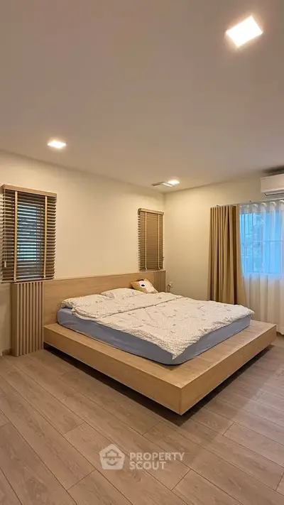 Spacious modern bedroom with wooden flooring and large windows for natural light.