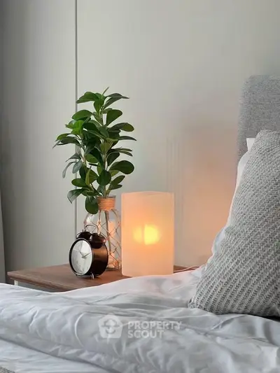 Cozy bedroom with stylish bedside table, modern lamp, and lush plant for a serene ambiance.
