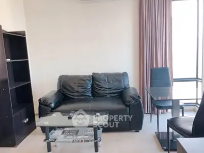 Modern living room with black leather sofa and glass coffee table in a bright apartment.