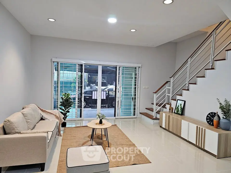 Spacious modern living room with elegant staircase and large sliding doors to patio.