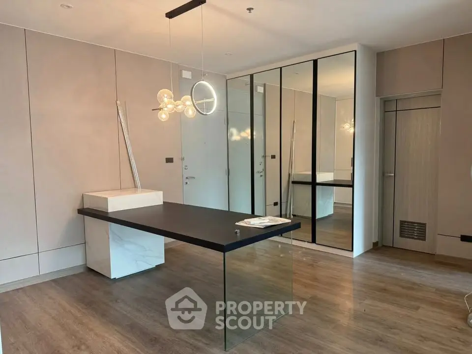 Modern study room with sleek glass desk and stylish lighting in a contemporary apartment.