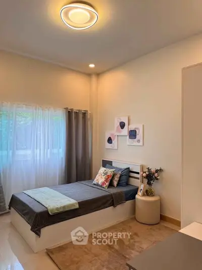 Cozy bedroom with modern decor and natural light, featuring a single bed and stylish artwork.