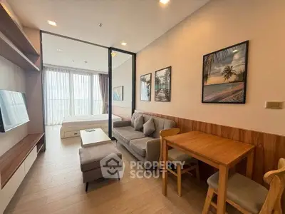 Modern living room with cozy seating and stylish decor, adjacent to a bright bedroom with large windows.