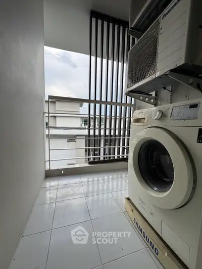 Modern balcony with washing machine and air conditioning unit in urban setting.