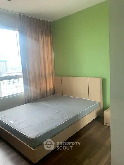 Cozy bedroom with green accent wall and large window offering city views