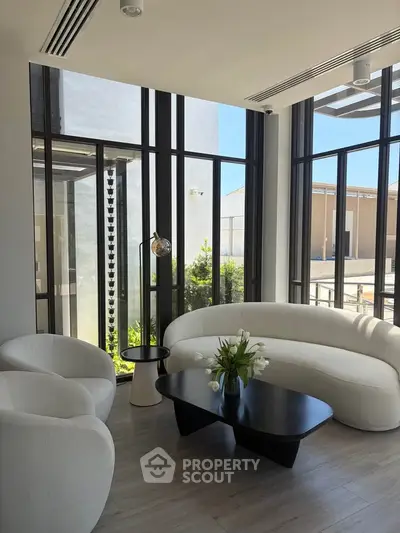 Modern living room with sleek furniture and large windows offering natural light and outdoor views.
