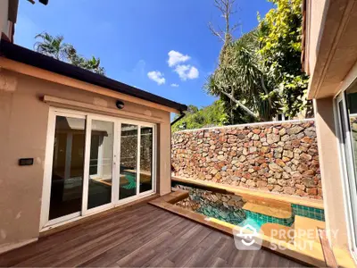 Charming private pool area with stone wall and wooden deck in a serene tropical setting.