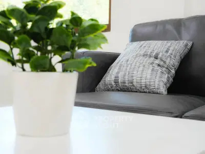 Modern living room with stylish gray sofa and decorative pillow, featuring a lush green plant on a white table.