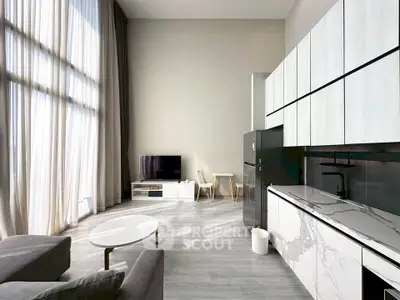 Modern living room with high ceilings and sleek kitchen design, featuring large windows and contemporary furniture.