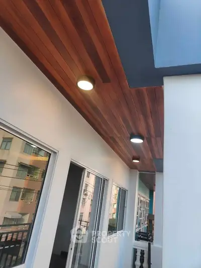 Modern balcony with wooden ceiling and recessed lighting in urban apartment building.